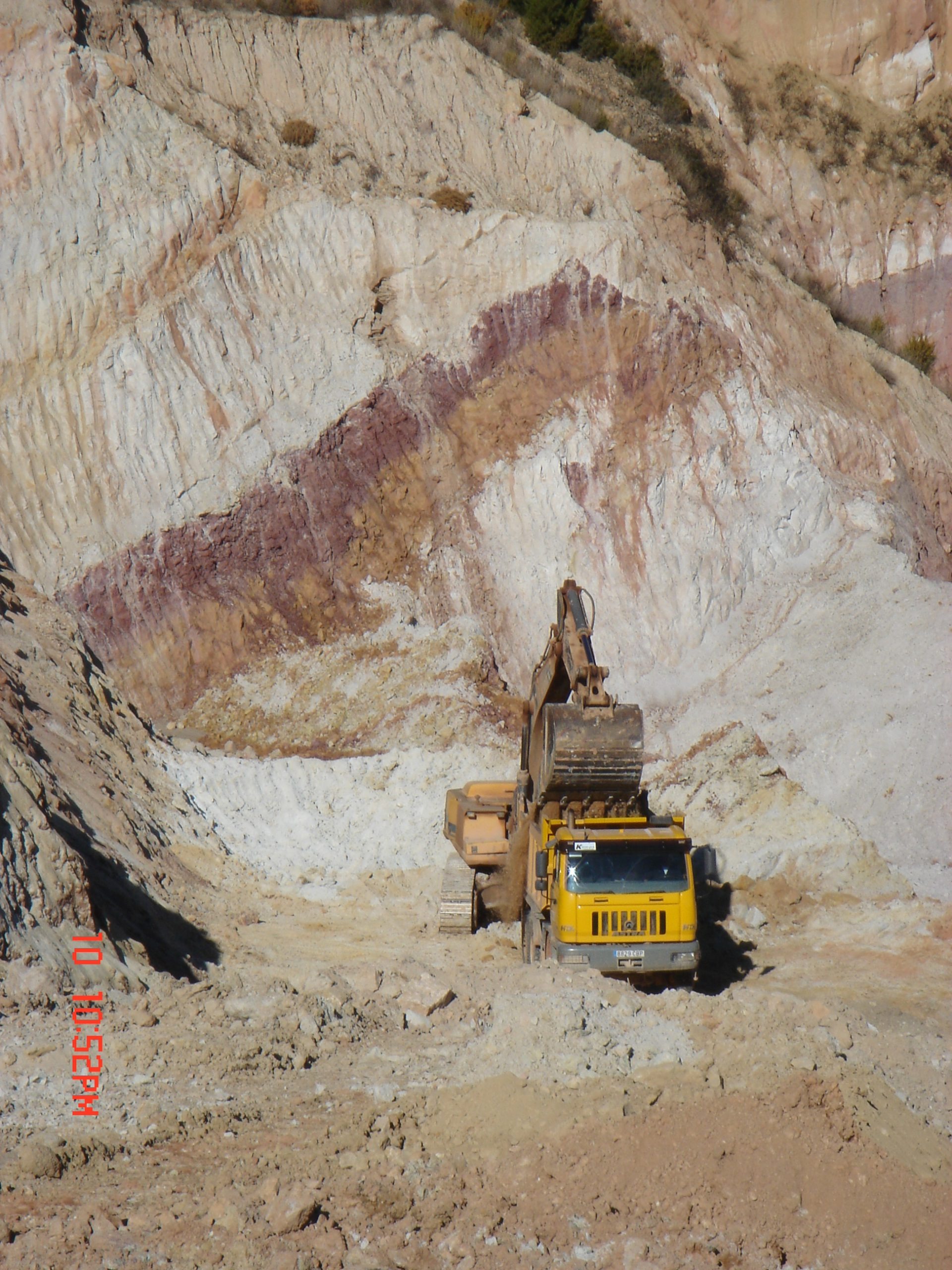 Excavadora cargando camión en cantera para la producción y purificación de materia prima para cristalería y cerámica